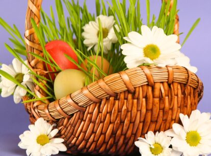 A basket filled with green grass and decorated with pastel-colored Easter eggs.