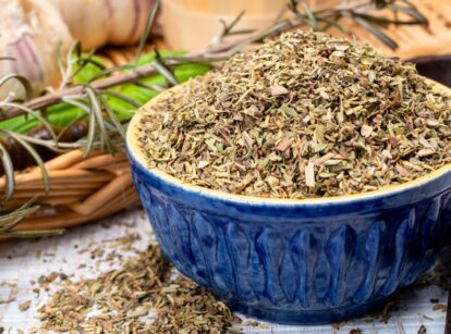 Herbes de Provence blend of dried herbs including savory, marjoram, rosemary, thyme, oregano, and lavender leaves in a blue ceramic bowl.