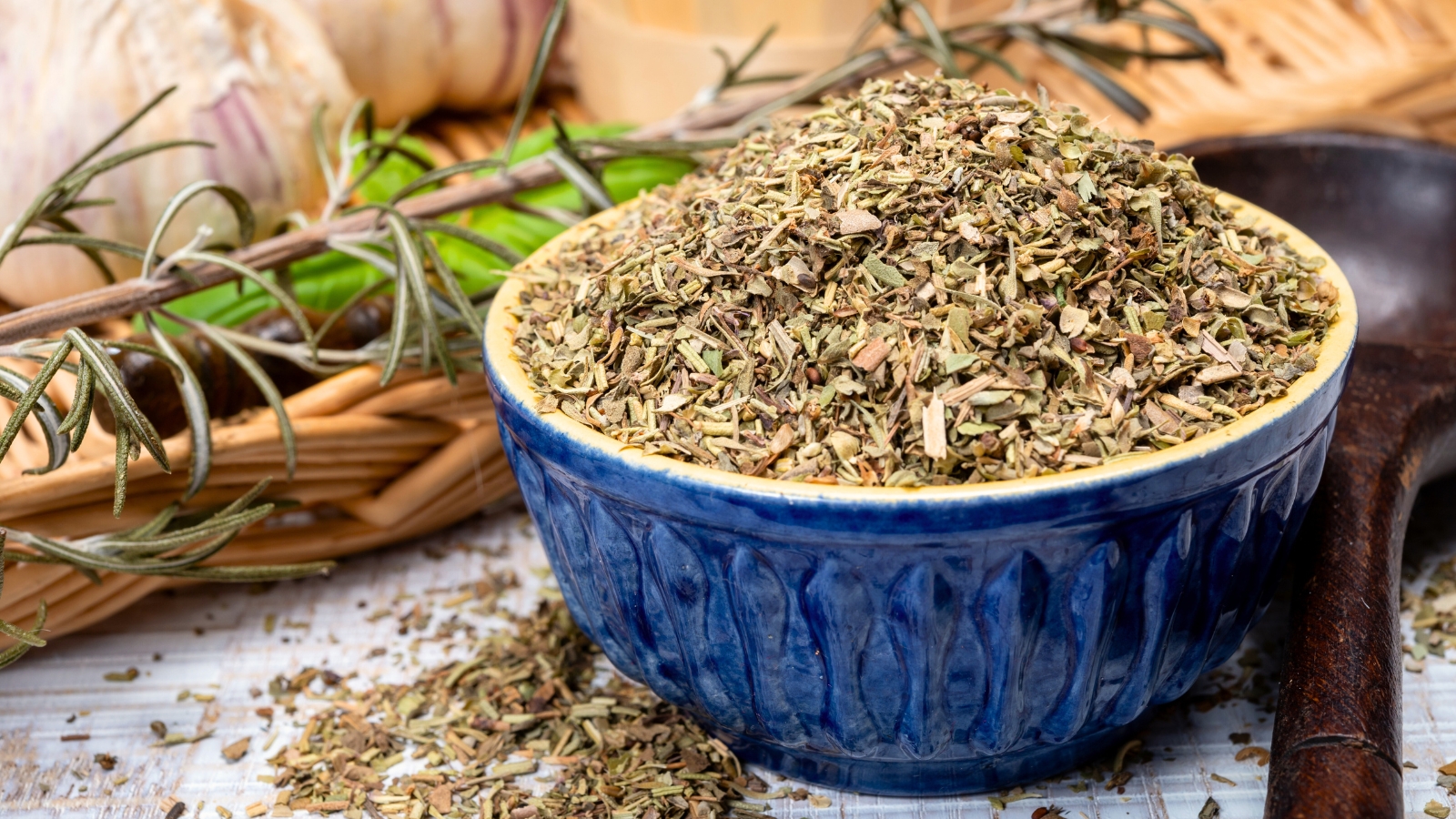 Herbes de Provence blend of dried herbs including savory, marjoram, rosemary, thyme, oregano, and lavender leaves in a blue ceramic bowl.