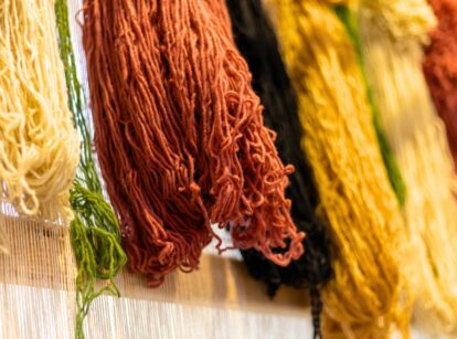 Wool fibers in various colors, dyed with natural dyes, hang from a loom.