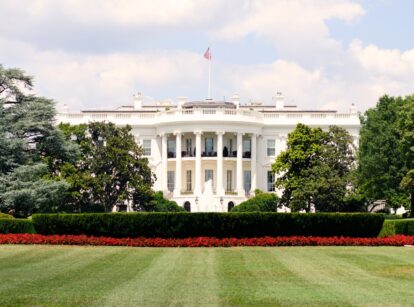 The White House in Washington, DC, surrounded by well-manicured garden beds with neatly trimmed lawns and ornamental plantings.