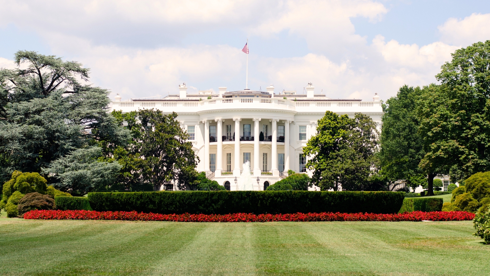 The White House in Washington, DC, surrounded by well-manicured garden beds with neatly trimmed lawns and ornamental plantings.