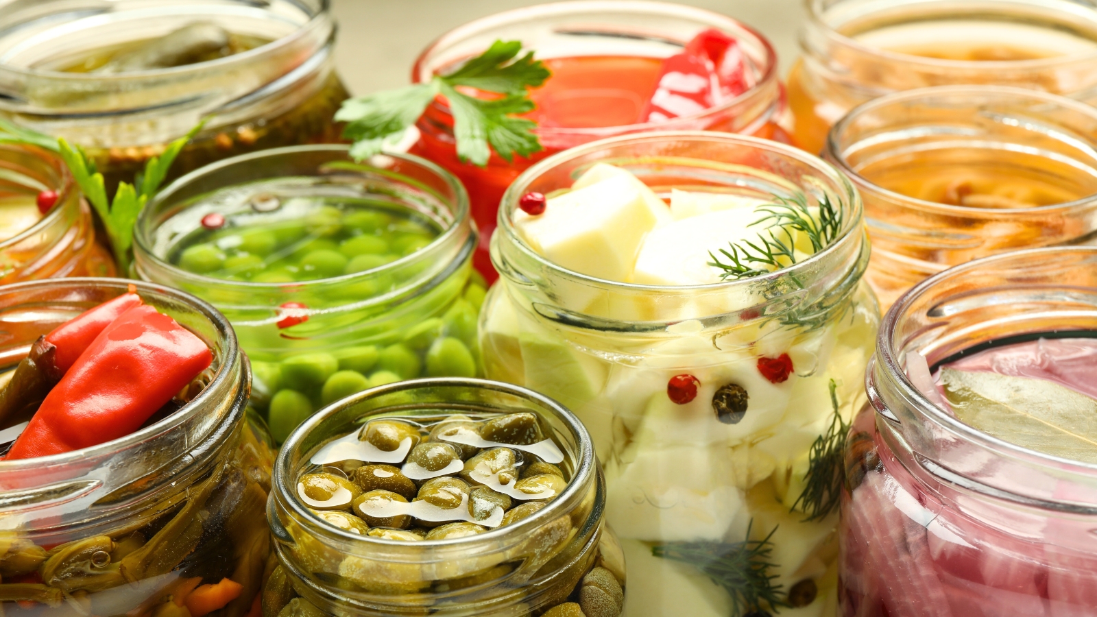 Close-up of various canned vegetables in jars with open lids, revealing their contents.