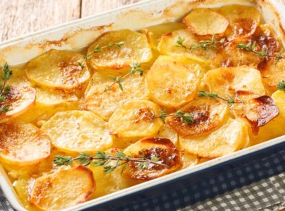 A baking sheet with scalloped potatoes topped with fresh thyme, baked to a golden brown.