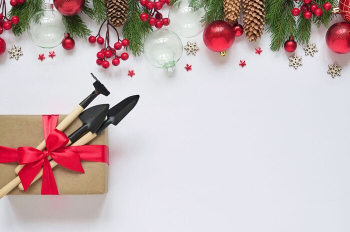 A shot of garden tools on top of a gift box alongside yuletide decorations that shows holiday seed gifts