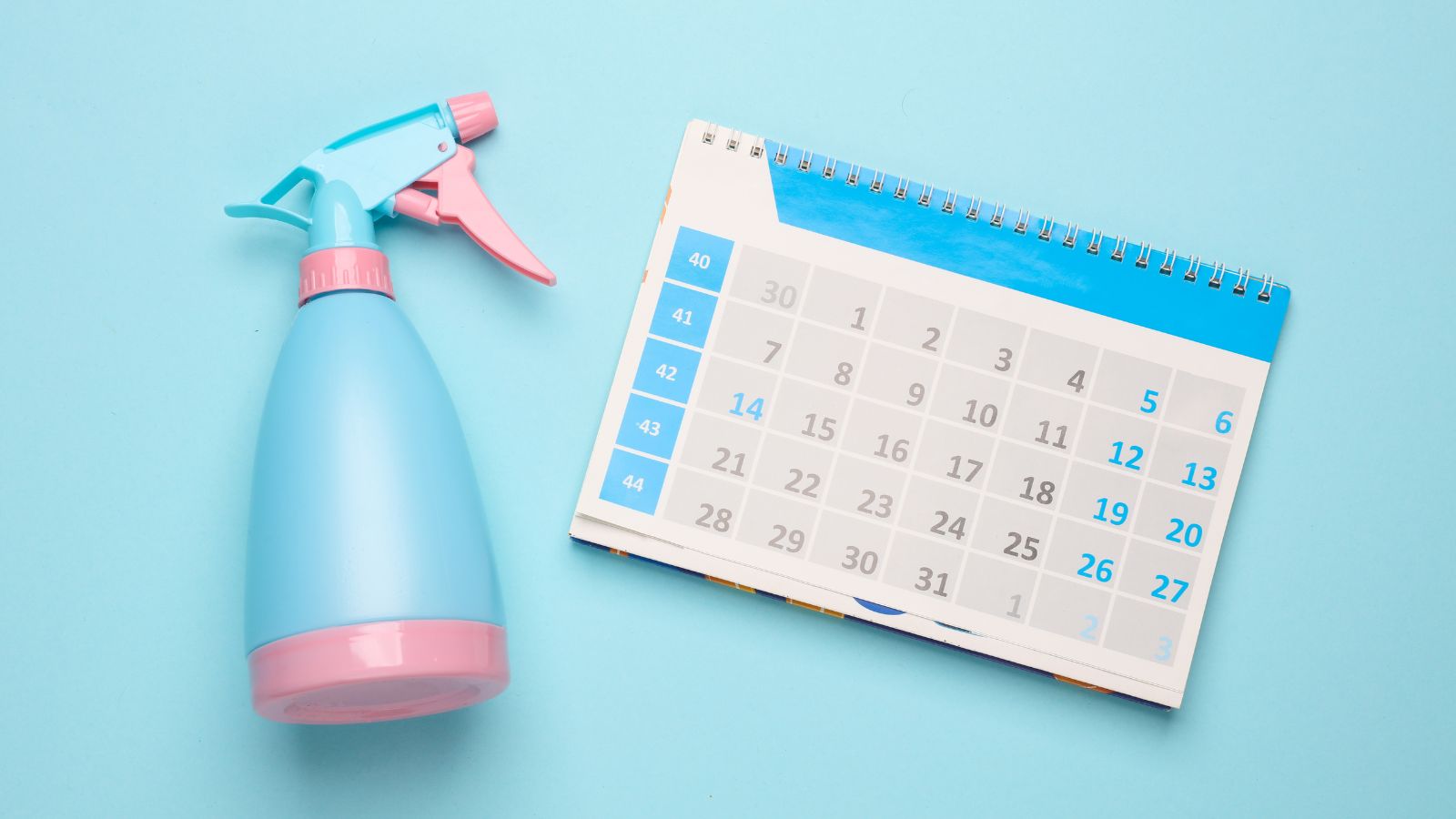 An overhead flat-lay shot of a calendar beside a spray bottle placed on top of a blue surface