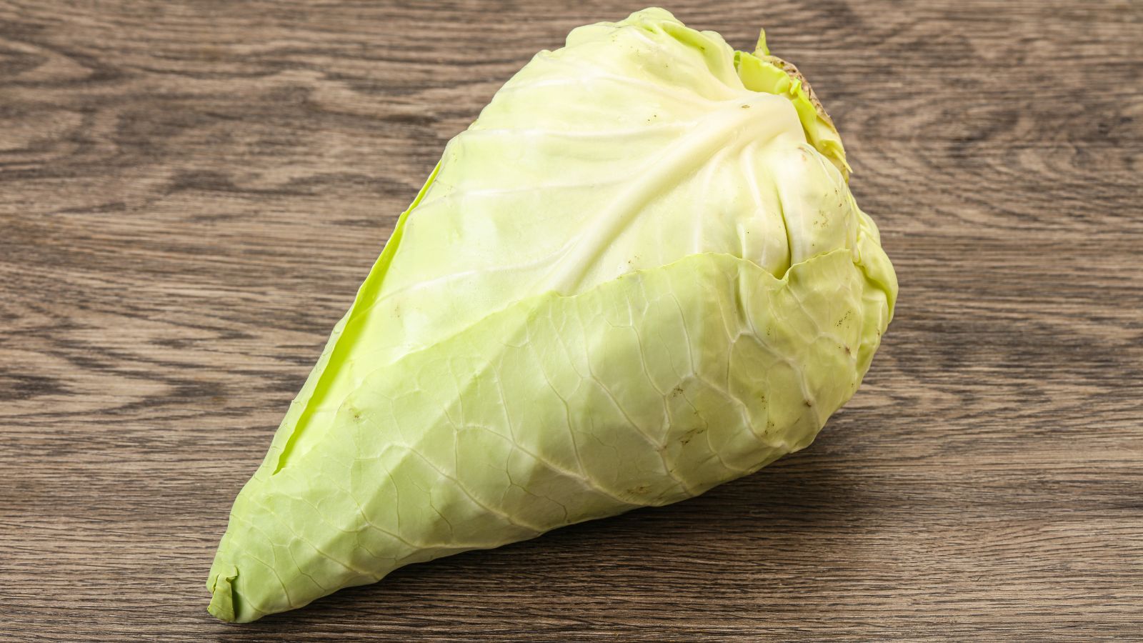 A close-up shot of a Caraflex Cabbage appearing a light yellow green with veiny leaves wrapped into a cone-like form