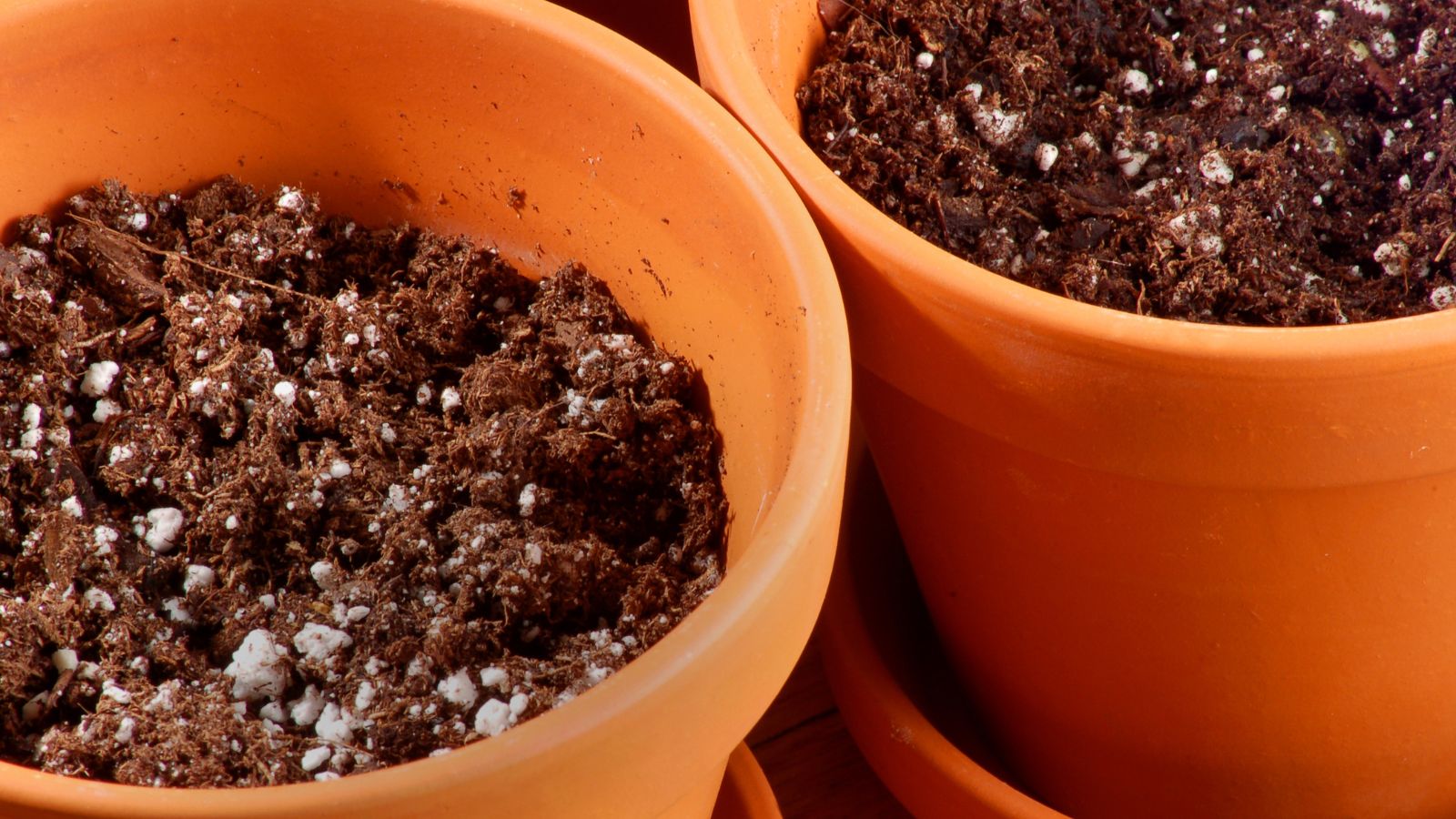 An overhead close-up shot of terracotta pots with a soil mix in a well lit area